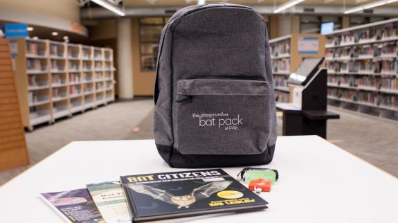A backpack placed on a table in a library, with shelves of books visible in the background.