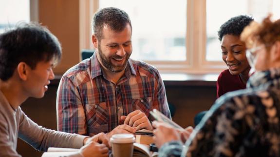 A diverse group of people engaged in discussion while sitting around a table with open books in front of them.