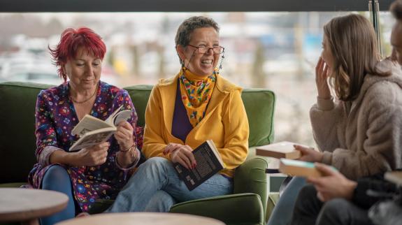 Three women sit comfortably on a couch, discussing the book they are reading and sharing a moment of literary enjoyment.