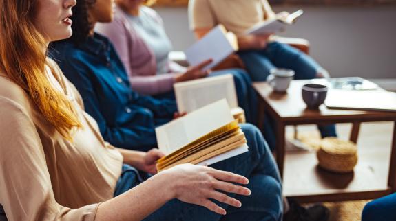 Diverse group of people sitting in a circle, holding open books, actively talking and exchanging thoughts, creating a sense of community and engagement.