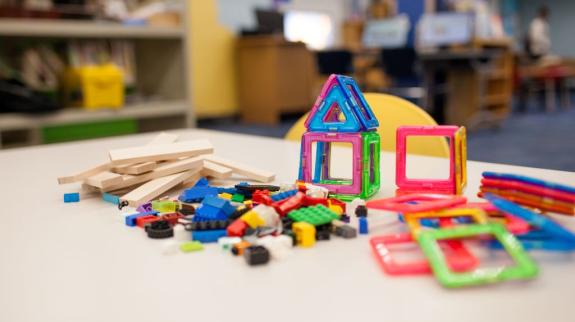 A colourful assortment of Keva Planks, Lego, and Magformers lying on a beige desk with library stacks in the background.