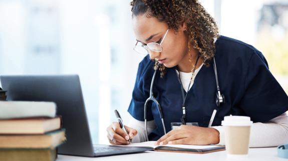 A healthcare worker in scrubs typing on a laptop, emphasizing her dedication to patient care and documentation.