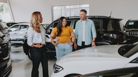 A dad and daughter explore a car showroom, discussing options and reviewing consumer reports for their next vehicle purchase