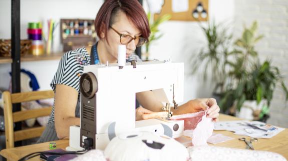 A woman is engaged in sewing a stuffed animal, highlighting her artistic flair and dedication to handmade crafts.