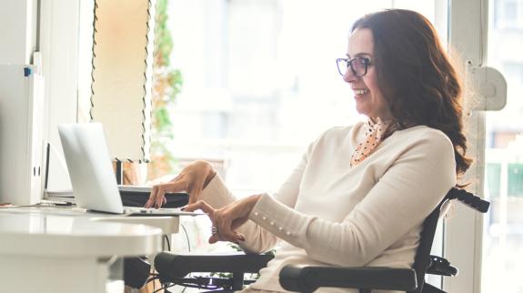 A woman using a laptop while seated in her wheelchair, representing empowerment and accessibility in the digital age.