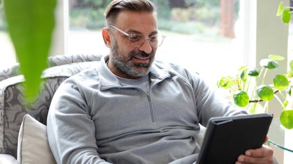A man sitting comfortably in a chair, relaxed and engaged with his tablet.