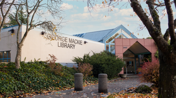 A leafy tree stands in front of the George Mackie Langley Library in North Delta, showcasing its vibrant exterior.
