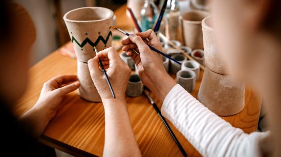 Two individuals collaborate on painting small flower pots sharing in a cozy workspace.