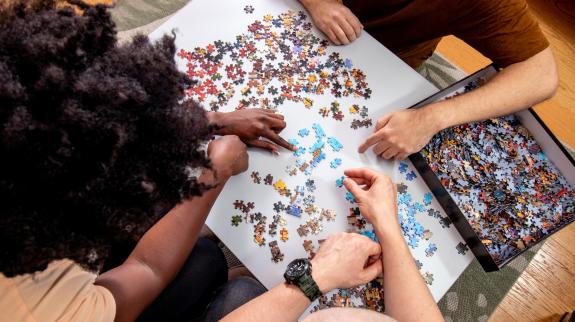 A high level view of three adults working together to complete a puzzle.
