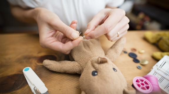 A person is engaged in sewing a teddy bear, skillfully fixing the soft toy with love and attention to detail.