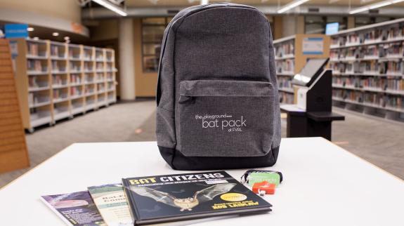 An FVRL Bat Pack sits on a table in the library. The kit includes a backpack with a bat detector and information about bats. 