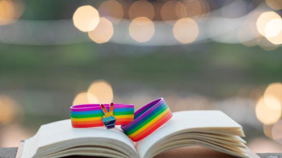 Rainbow wristband celebrating lgbtqia+ groups sit atop a library book with a defocused background.