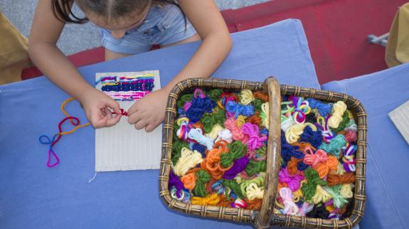 Child girl learning to use cardboard weaving loom.