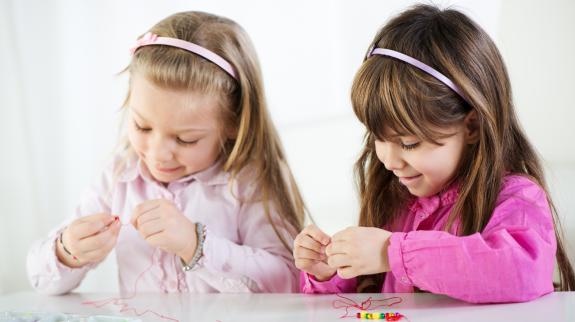 Two little girls making beaded friendship bracelets. 