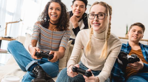 A enthusiastic multi-ethnic group of two teen girls, and two teen boys holding video game controllers.