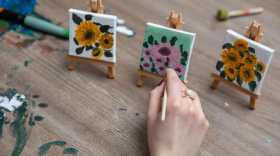 A hand paints beautifully handpainted artwork on small canvases, displaying vibrant floral designs on artist easels.