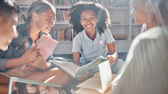 A diverse group of tweens sitting on the library floor, engaged in an animated discussion about the books they are reading.