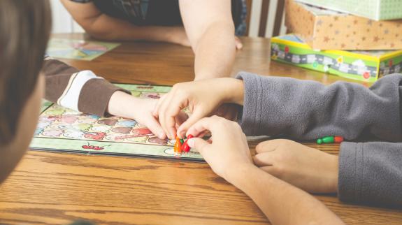 Image of multiple children's hands playing a board game together.