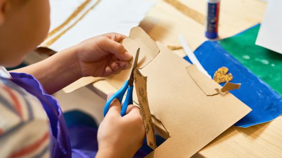 High angle portrait of unrecognizable little boy cutting paper in arts and crafts class making handmade gift.