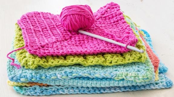 Crocheted dishcloths, with a hook and a ball of yarn.