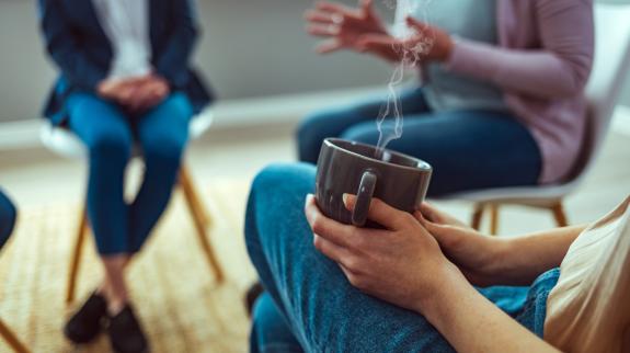Close-up view of hands holding a cup of coffee in a group conversation setting.
