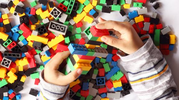 Close up of child's hand playing plastic toy building blocks, top view from above.