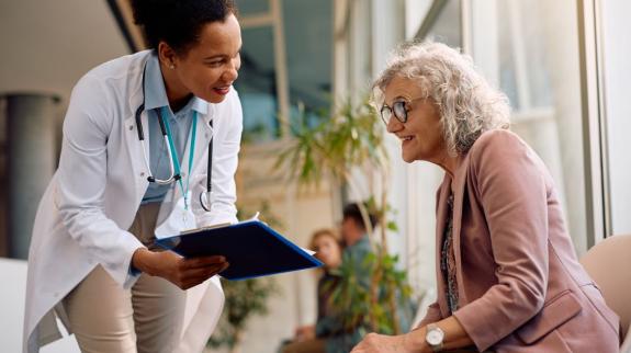 Smiling senior woman and her doctor going through paperwork in hallway at medical clinic.