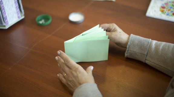 A pair of hands creates a green accordion book craft against the backdrop of a brown table top.