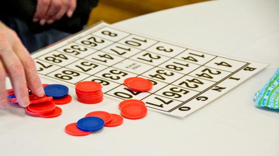 A bingo card, chips, and the fingers of an older individual suggest this bingo game is being played in a senior center.