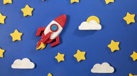 Space rocket and stars made with play clay on blue background.
