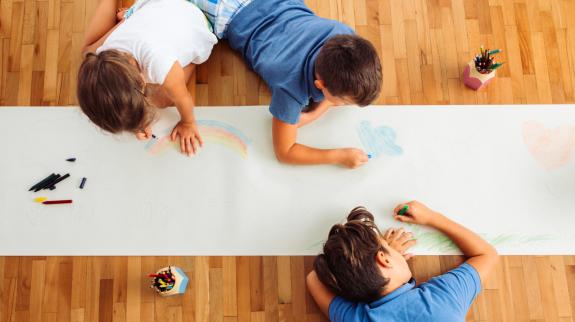 Above shot of group of children drawing on the white paper with colorful crayons.