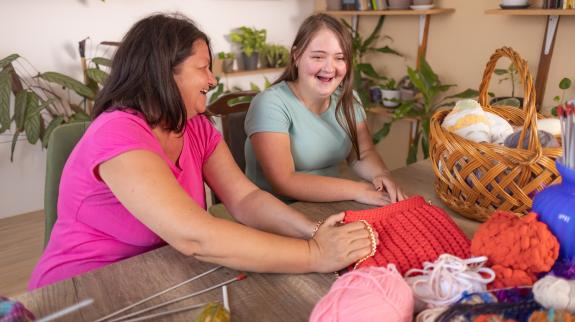 Two adult women collaborate on knitting a beautiful bag.