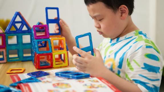 Young boy builds using magnetic Magformer pieces.