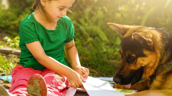 Young girl reading to a German Shepard dog outside on a mat.