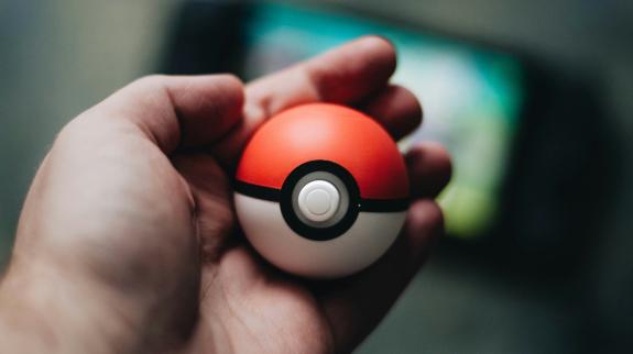 A pale hand holds a Poké-ball.