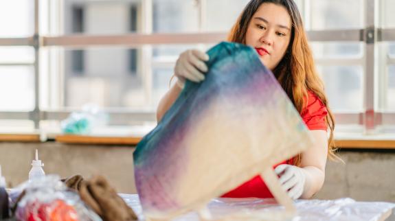 A young woman is making tie dye tote bag indoors.