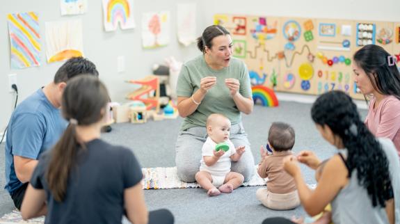 A small group of parents and their babies, participate in a sign language class together. 