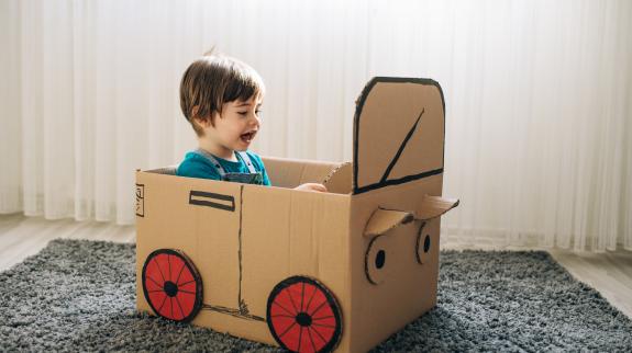 Little boy plays in the cardboard car.