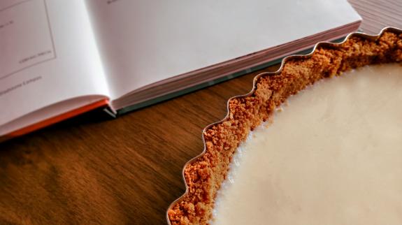 A freshly baked tart lays on a table by an open cookbook.
