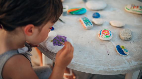 Little girl paints rocks using different colors.
