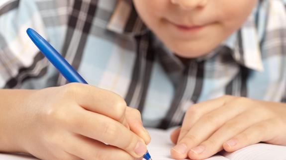 Young boy doing his homework with a blue pen.