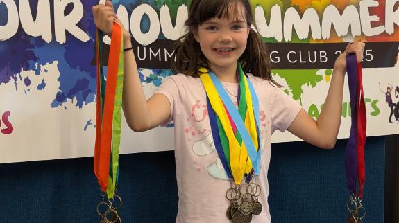 A smiling girl holds up bundles of Summer Reading Club medals.