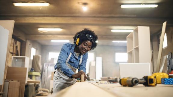 One African-American female carpenter working with wood in her workshop.