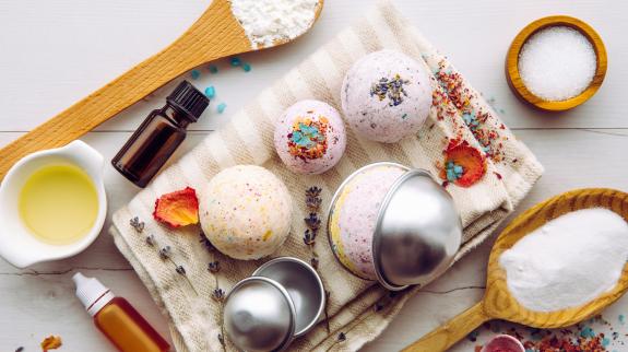 Making bath fizz bombs. All the ingredients on table on wood spoons: cornstarch, essential oil, dye, citric acid, baking soda, dry herbs, round metal pressing molds.