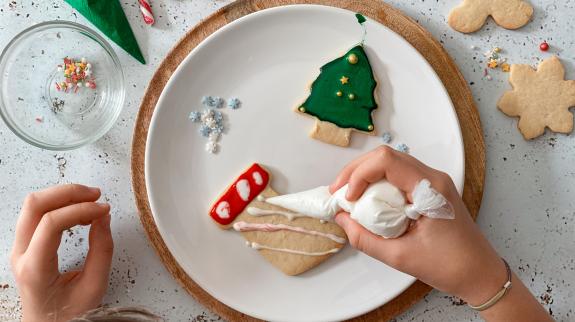 Table top view of teen girl hands decorating homemade Christmas cookies.