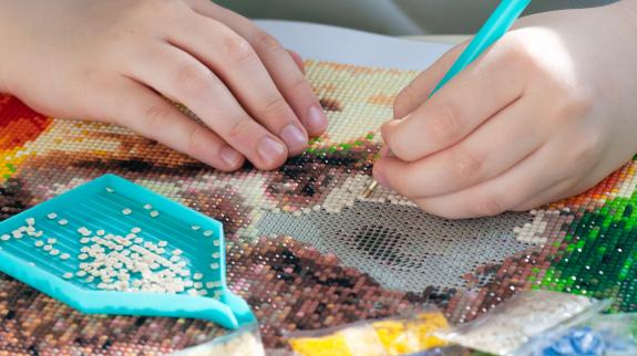 Close up of hands working on a diamond art mosaic project.