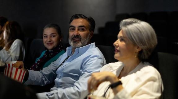 People enjoying popcorn while watching a movie in a cozy cinema, sharing smiles and laughter in a lively atmosphere.