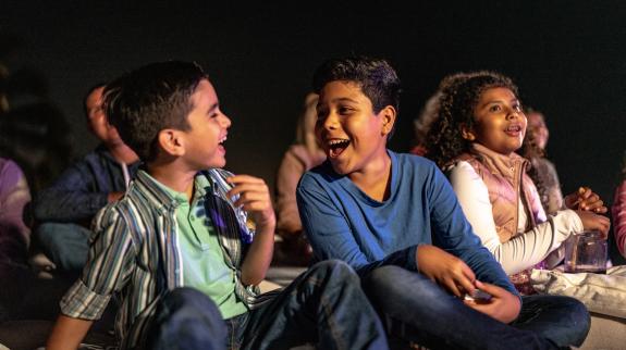 Young kids sitting on the library floor, joking around, and enjoying a movie.