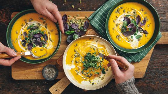 Men eating Vegan Creamy Roasted Pumpkin Soup on wooden background.
