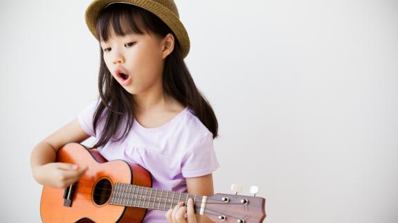Young Asian girl singing and playing ukulele.